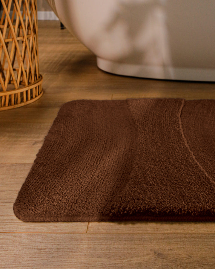 Badteppich Marc Braun runde Matte im Badezimmer vor Badewanne, Strukturmuster im Flor auf Holzboden sichtbar