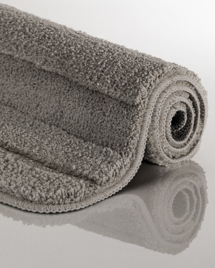 Badteppich Marc Basalt Grau aufgerollt auf hellem Hintergrund, Seitenansicht zeigt Florhöhe und Teppichkante