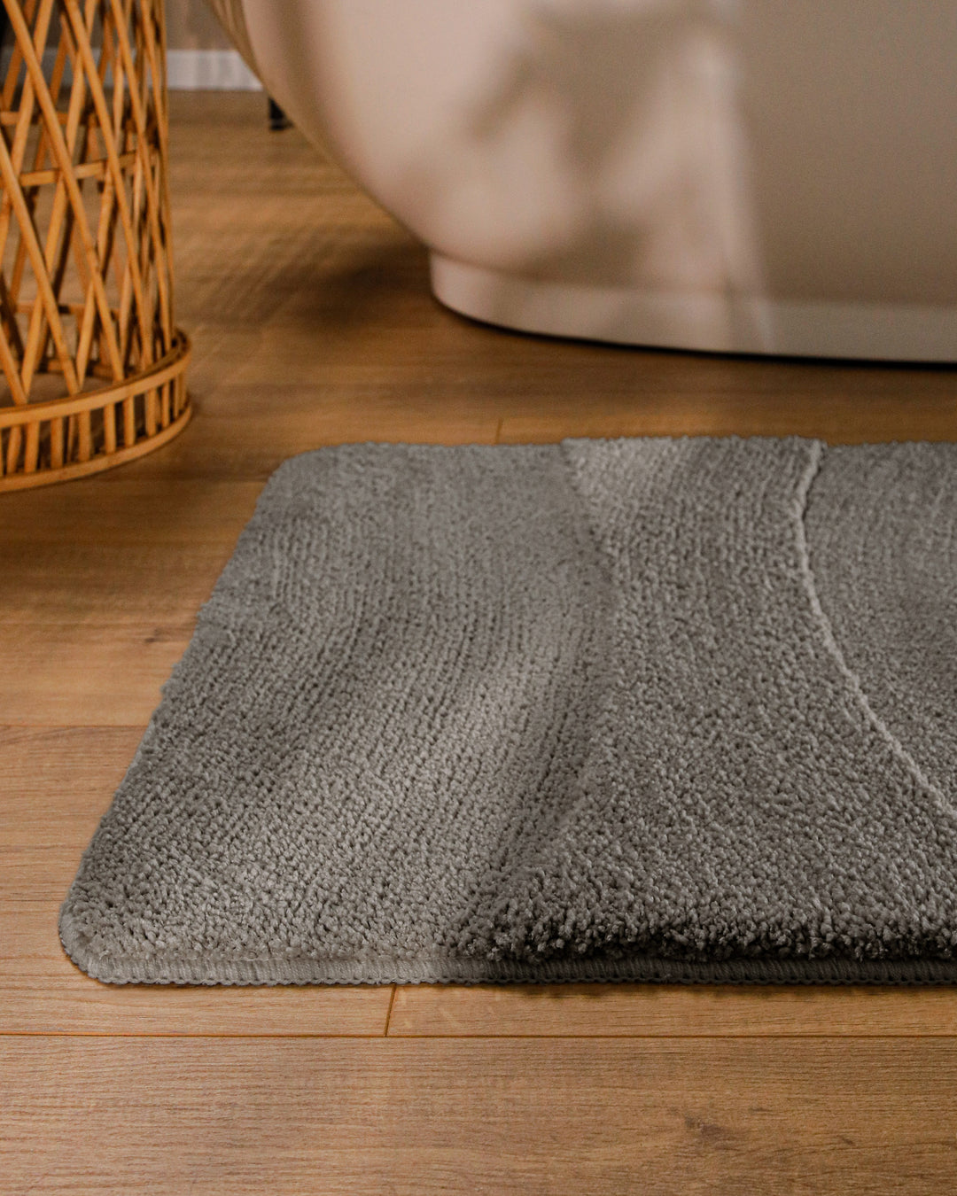 Badteppich Marc Basalt Grau runde Matte im Badezimmer vor Badewanne, Strukturmuster im Flor auf Holzboden sichtbar