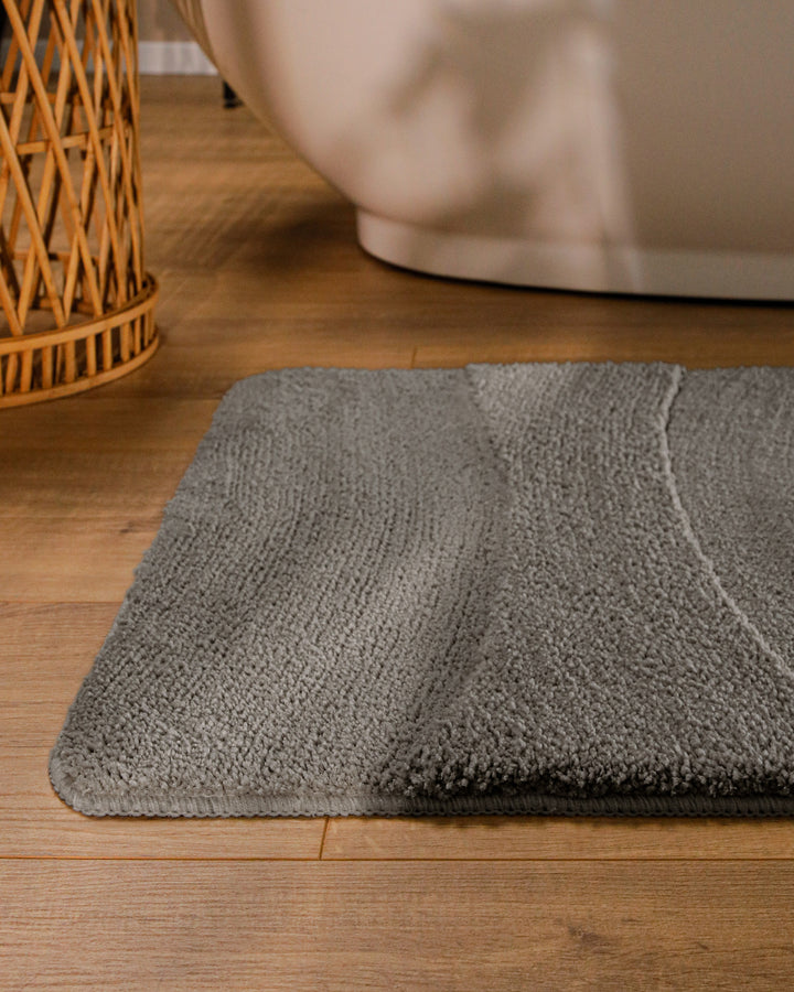 Badteppich Marc Basalt Grau runde Matte im Badezimmer vor Badewanne, Strukturmuster im Flor auf Holzboden sichtbar