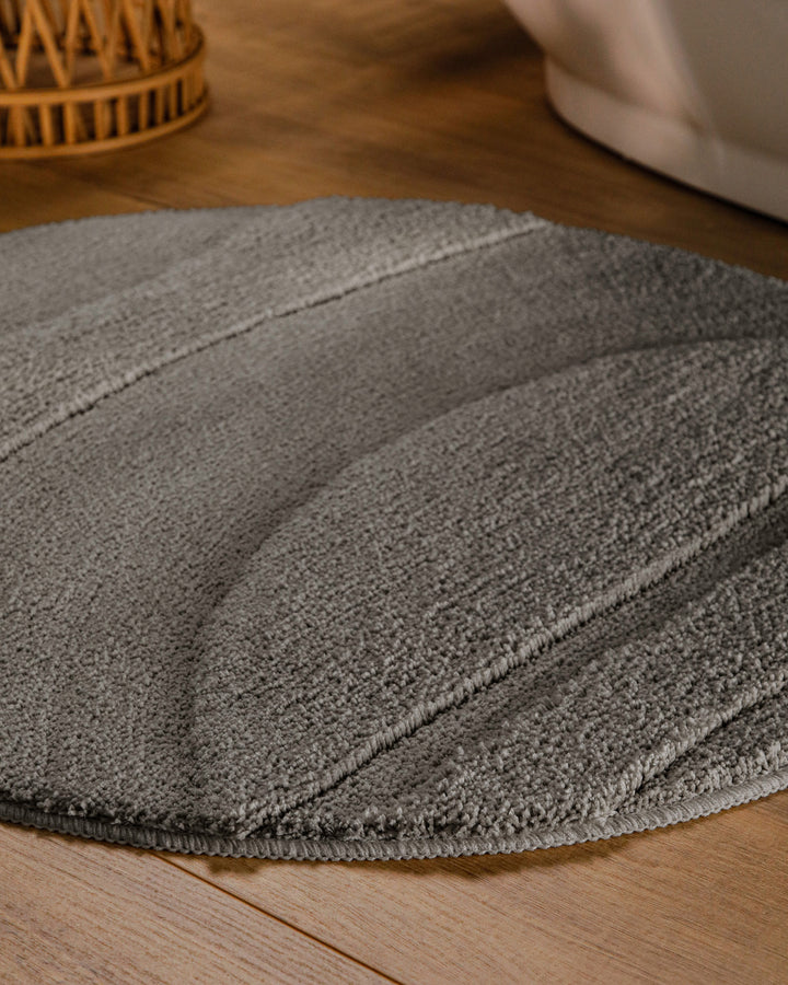 Badteppich Marc Basalt Grau rund im Badezimmer auf Holzboden neben Badewanne, Florstruktur und Linienrelief erkennbar