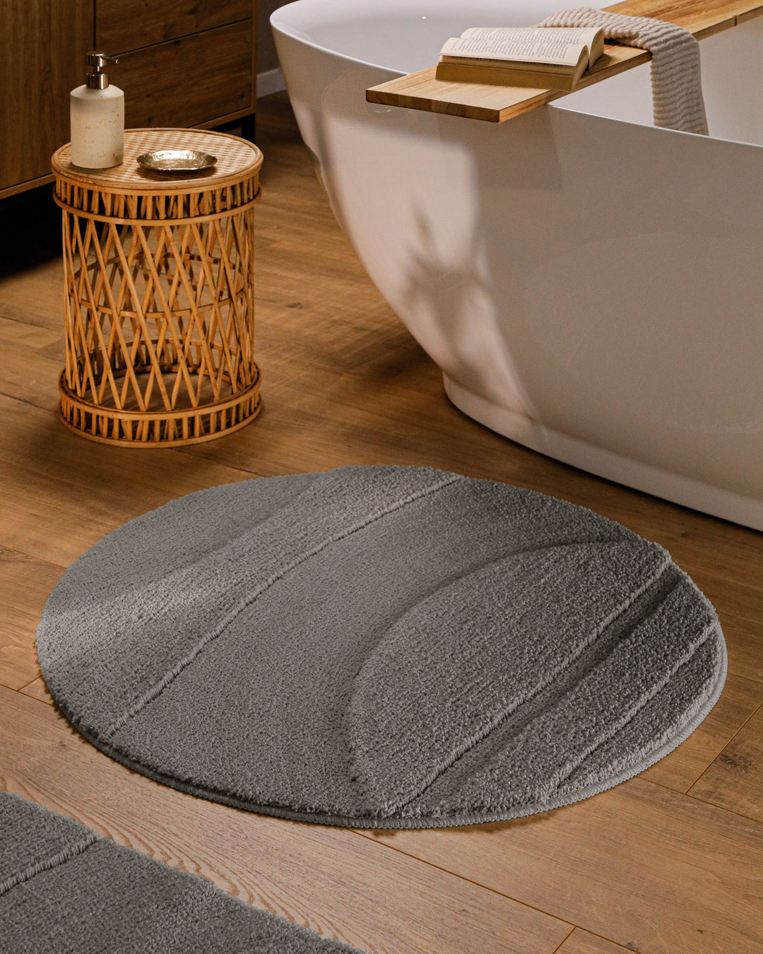 Runder Badteppich Marc Basalt Grau im Badezimmer vor Badewanne auf Holzboden, strukturiertes Linienrelief im Flor sichtbar