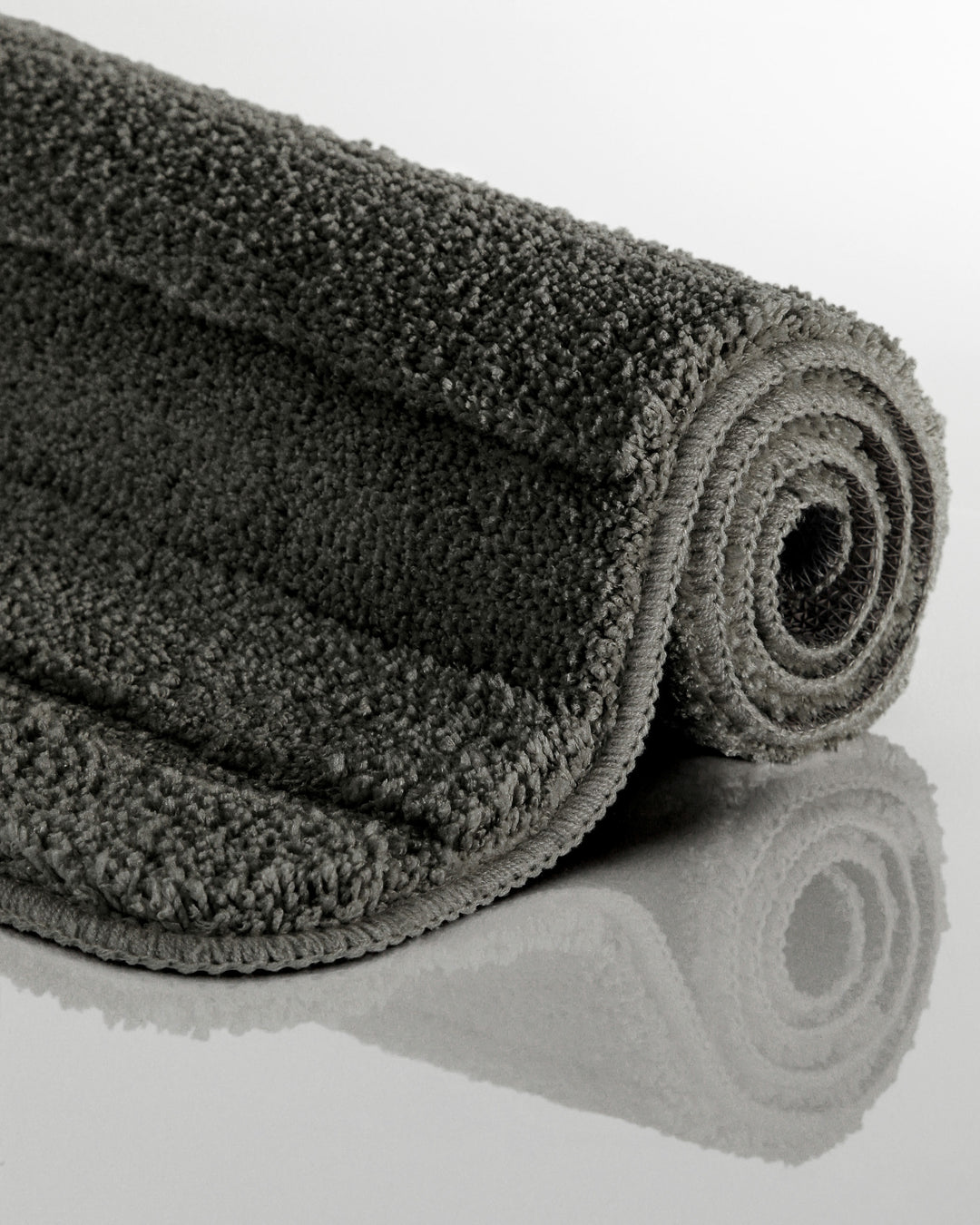 Badteppich Marc Anthrazit Grau aufgerollt auf hellem Hintergrund, Seitenansicht zeigt Florhöhe und Teppichkante