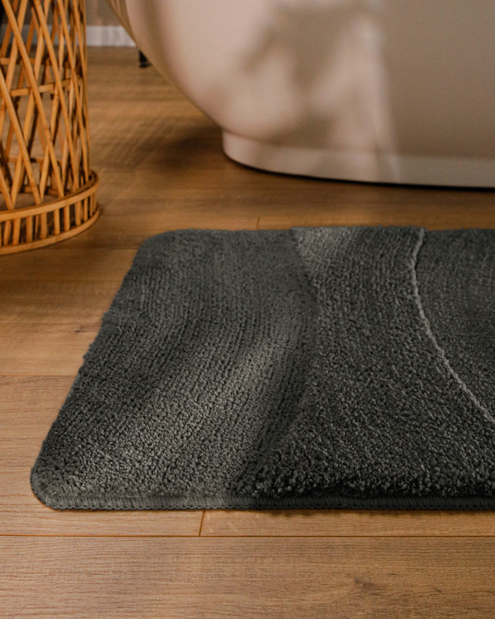 Badteppich Marc Anthrazit Grau runde Matte im Badezimmer vor Badewanne, Strukturmuster im Flor auf Holzboden sichtbar