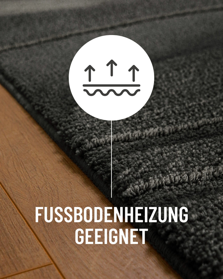 Badteppich Marc Anthrazit Grau Detail auf Holzfußboden mit Symbol für Fußbodenheizung, Nahaufnahme von Flor und Teppichkante