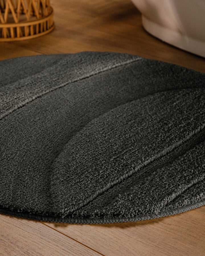 Badteppich Marc Anthrazit Grau rund im Badezimmer auf Holzboden neben Badewanne, Florstruktur und Linienrelief erkennbar