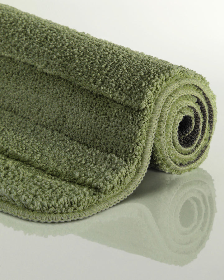 Badteppich Marc Reseda Grün aufgerollt auf hellem Hintergrund, Seitenansicht zeigt Florhöhe und Teppichkante