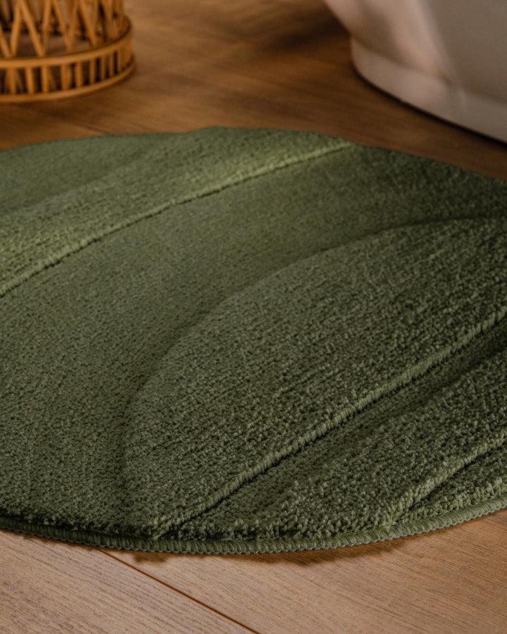 Badteppich Marc Kiefer Grün rund im Badezimmer auf Holzboden neben Badewanne, Florstruktur und Linienrelief erkennbar