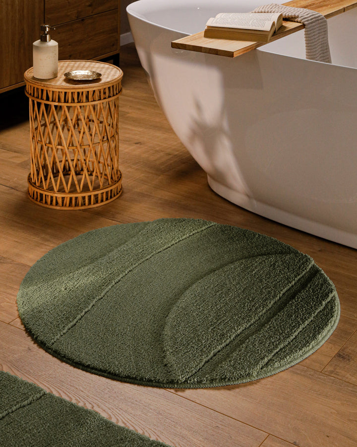 Runder Badteppich Marc Kiefer Grün im Badezimmer vor Badewanne auf Holzboden, strukturiertes Linienrelief im Flor sichtbar