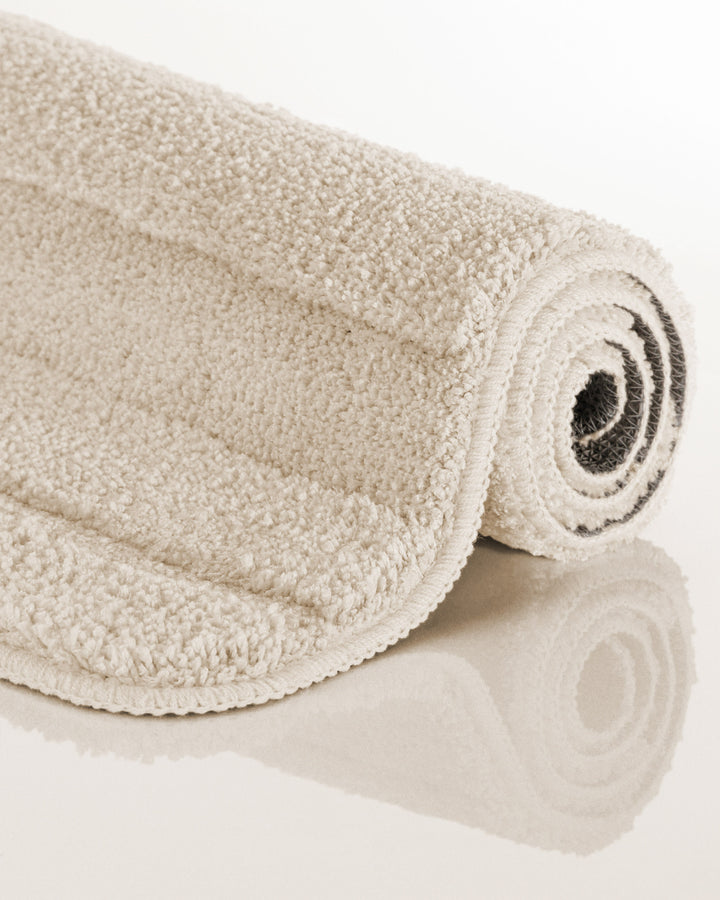 Badteppich Marc Creme Weiß aufgerollt auf hellem Hintergrund, Seitenansicht zeigt Florhöhe und Teppichkante