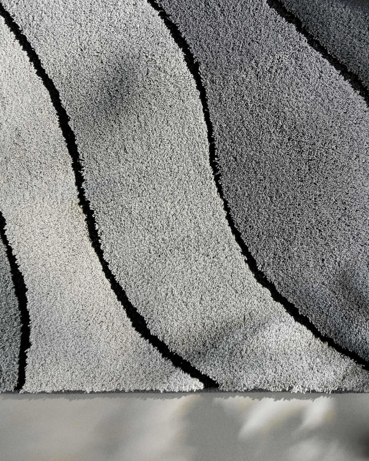 Makroaufnahme der Teppichoberfläche von oben – helle und mittlere Grautöne mit zwei schwarzen Wellenstreifen und feiner Florstruktur