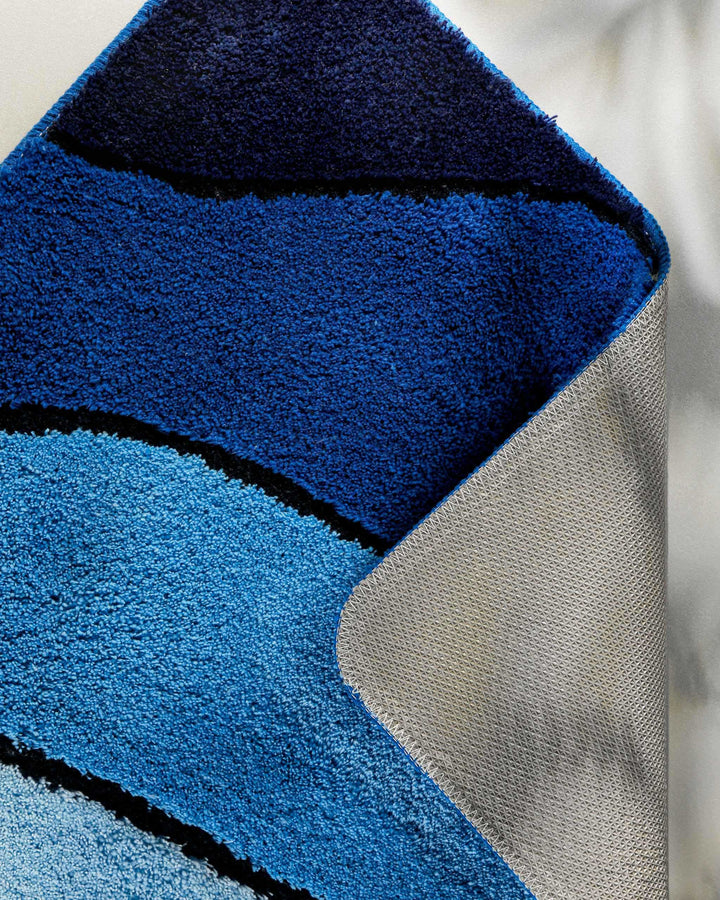 Nahaufnahme einer aufgeschlagenen Teppichkante – Flor in Dunkelblau mit Wellendetail auf der Vorderseite und sichtbarem beigem Textilrücken