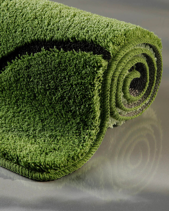 Badteppich Monte Cavo in Grün aufgerollt in Nahaufnahme – Querschnitt zeigt die Flordicke und die textile Rückenstruktur des grünen Badteppichs