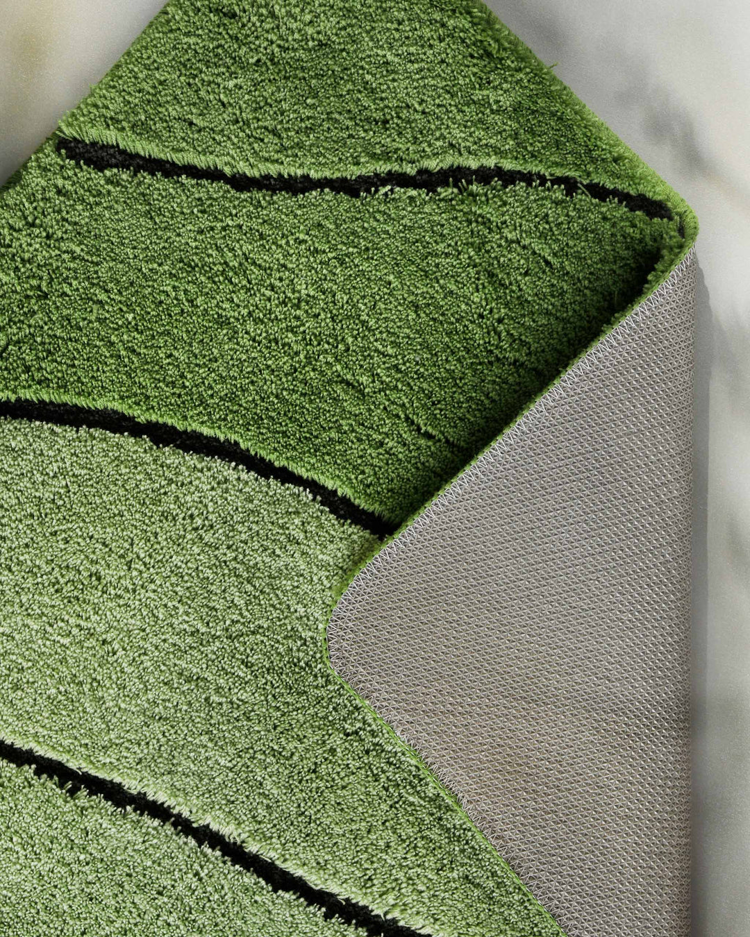 Nahaufnahme einer aufgeschlagenen Teppichkante – Flor in Dunkelgrün mit Wellendetail auf der Vorderseite und sichtbarem beigem Textilrücken