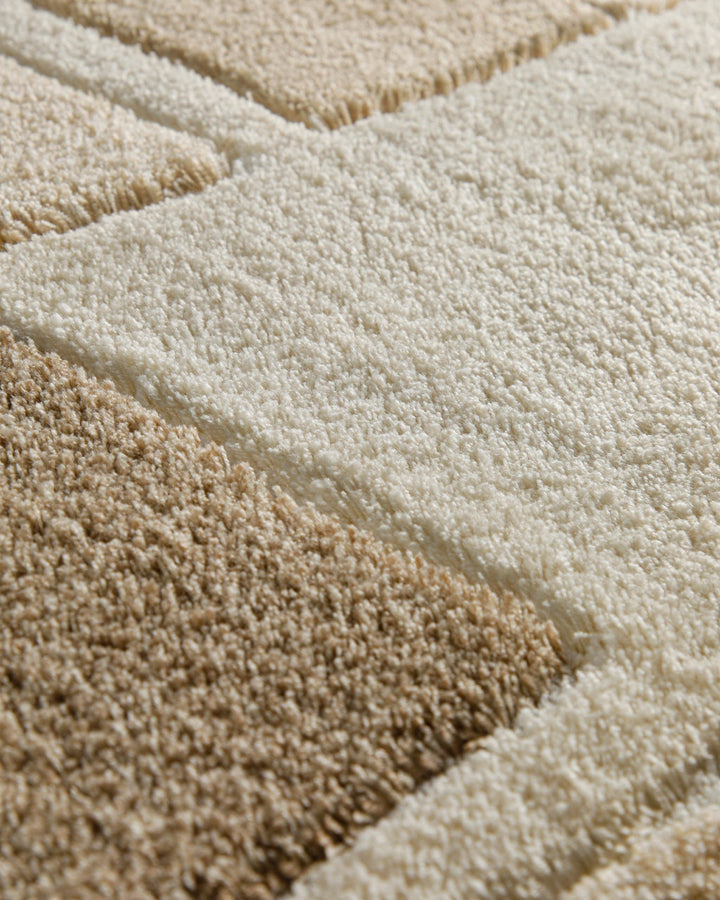 Extremnahaufnahme zweier aneinandergrenzender Florzonen des Badteppichs Villa Elba – cremefarbener Hochflor trifft auf sandbeige Blockfelder mit klar abgesetzter Naht