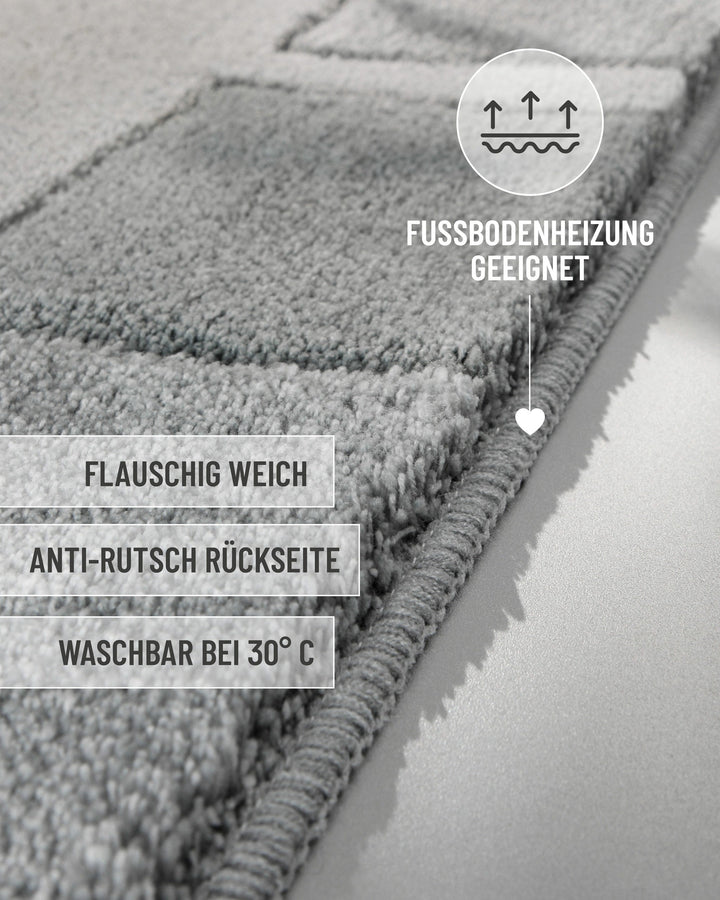 Seitliche Nahaufnahme der Teppichkante des Badteppichs Villa Elba in Grau mit eingeblendeten Produktvorteilen: flauschig weich, Anti-Rutsch-Rückseite, waschbar bei 30°C, Fußbodenheizung geeignet