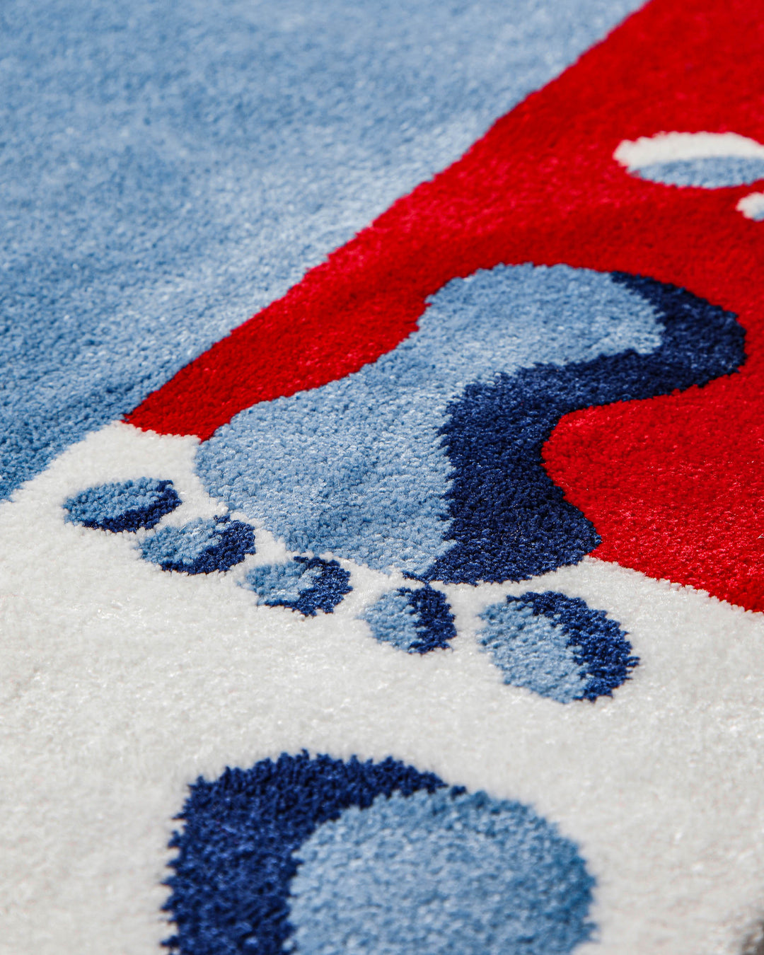 Detailaufnahme des Randmusters vom Kinderteppich Hand&Feet mit blauem Fußabdruck auf rotem Untergrund