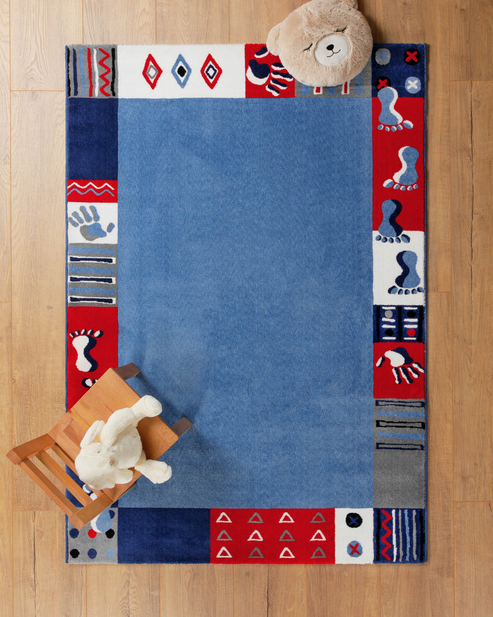 Kinderteppich Hand&Feet in Blau auf Holzboden mit Teddybär in der Ecke, Patchwork-Rand mit Fußabdrücken