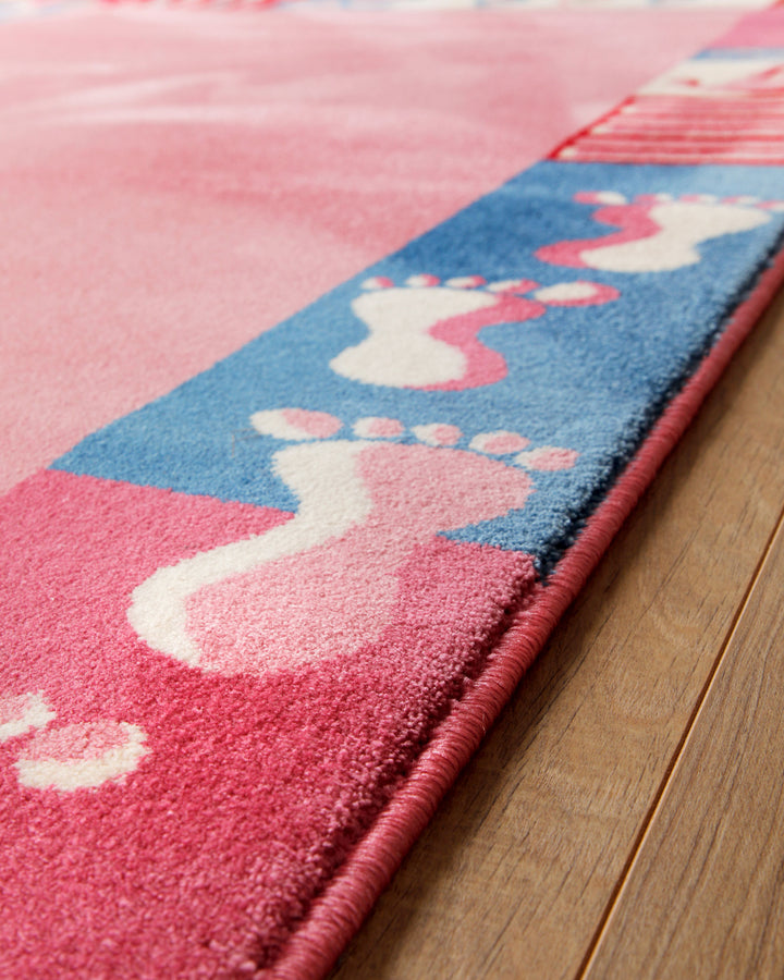 Kantenansicht des Kinderteppichs Hand&Feet auf Holzboden, Rand mit blauen und pinken Fußabdrücken diagonal fotografiert