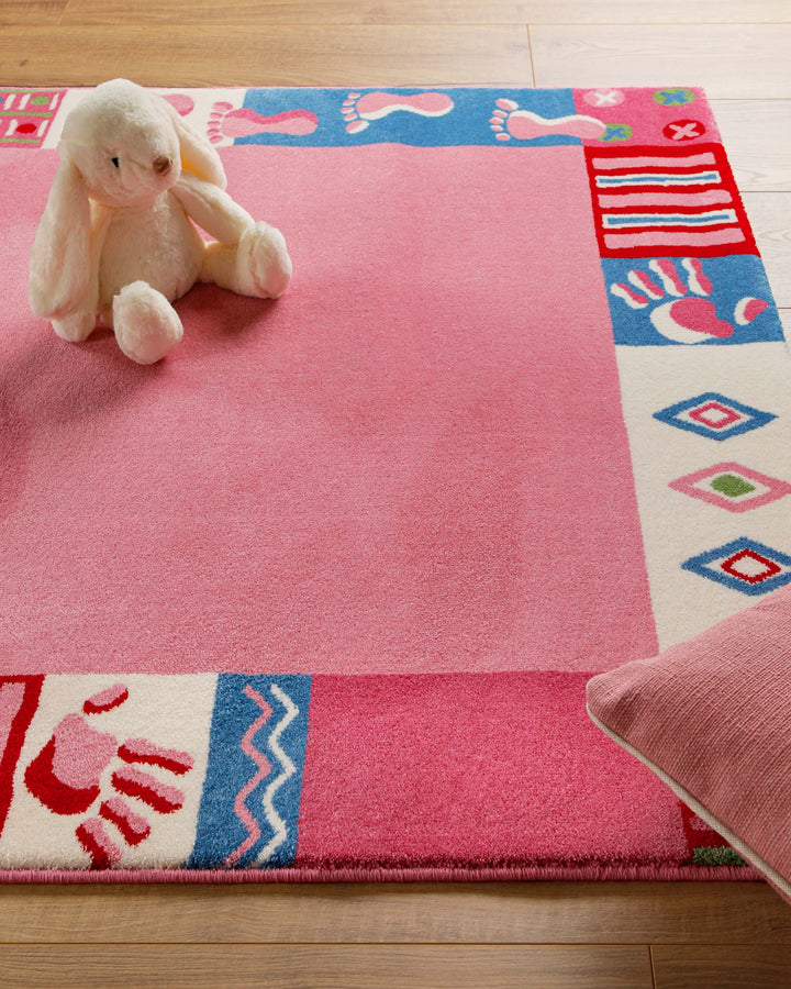 Ecke des Kinderteppichs Hand&Feet mit Teddybär als Deko, unifarbene pinke Mitte und gemusterter Rand mit Handabdrücken