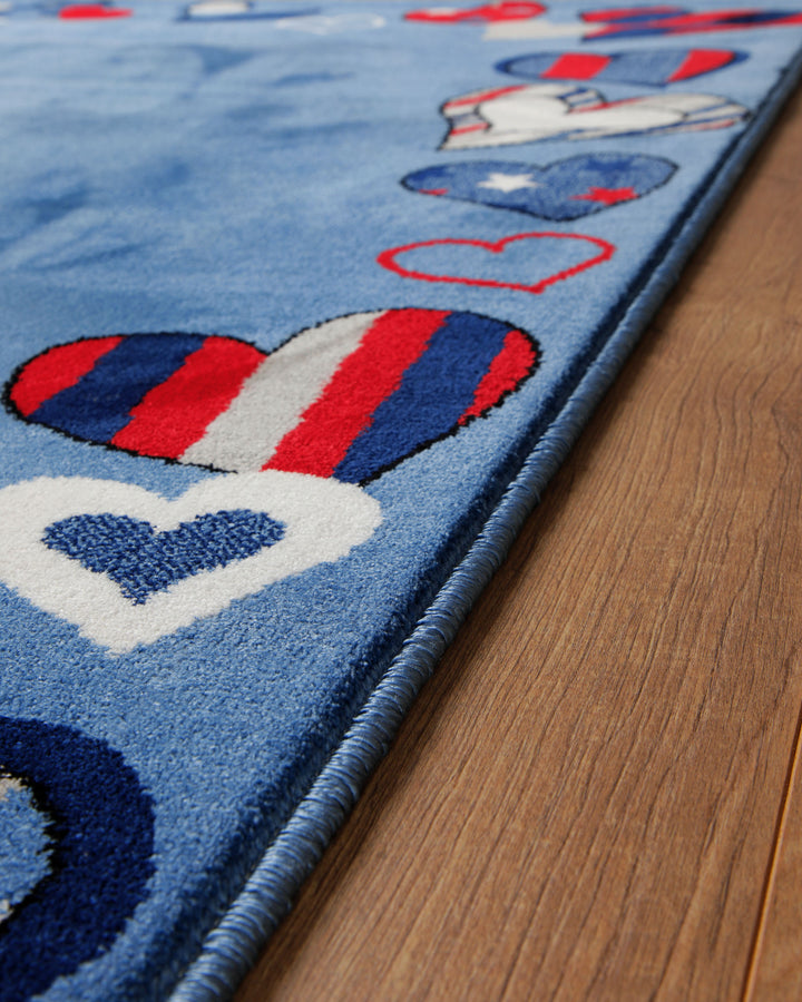 Kantendetail des Kinderteppichs Just Hearts auf Holzboden, Rand mit rot-blauen Herzen in Streifenmuster