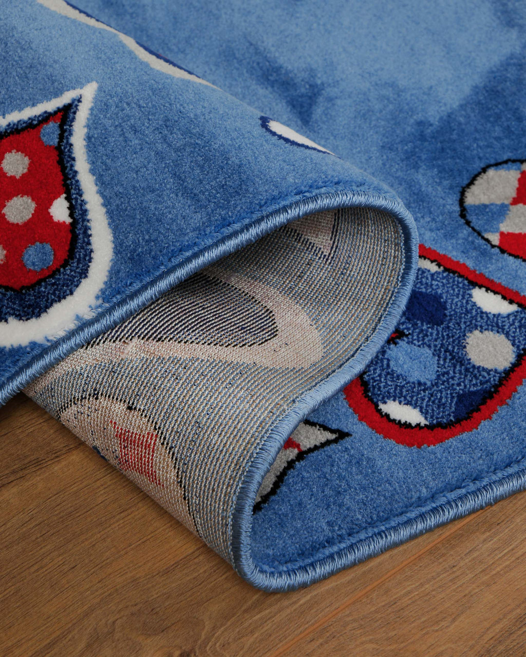 Kinderteppich Just Hearts, umgeschlagene Ecke zeigt Teppichrücken und blauen Rand mit Herz-Motiv auf Holzboden