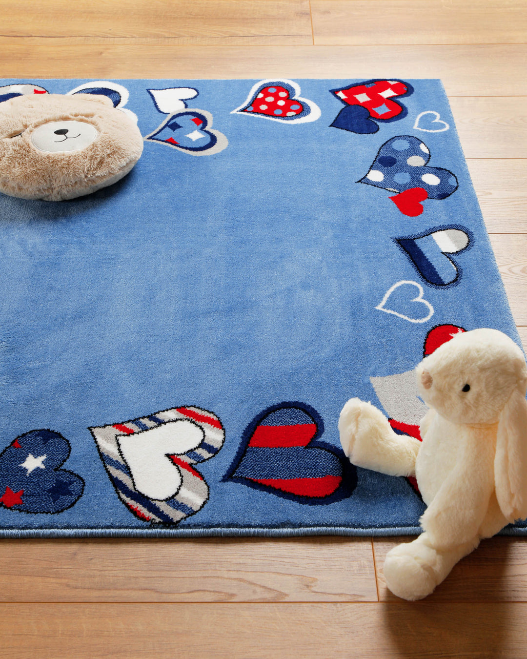 Ecke des Kinderteppichs Just Hearts mit Teddybär als Deko, unifarbene blaue Mitte und gemusterter Rand mit Herzen