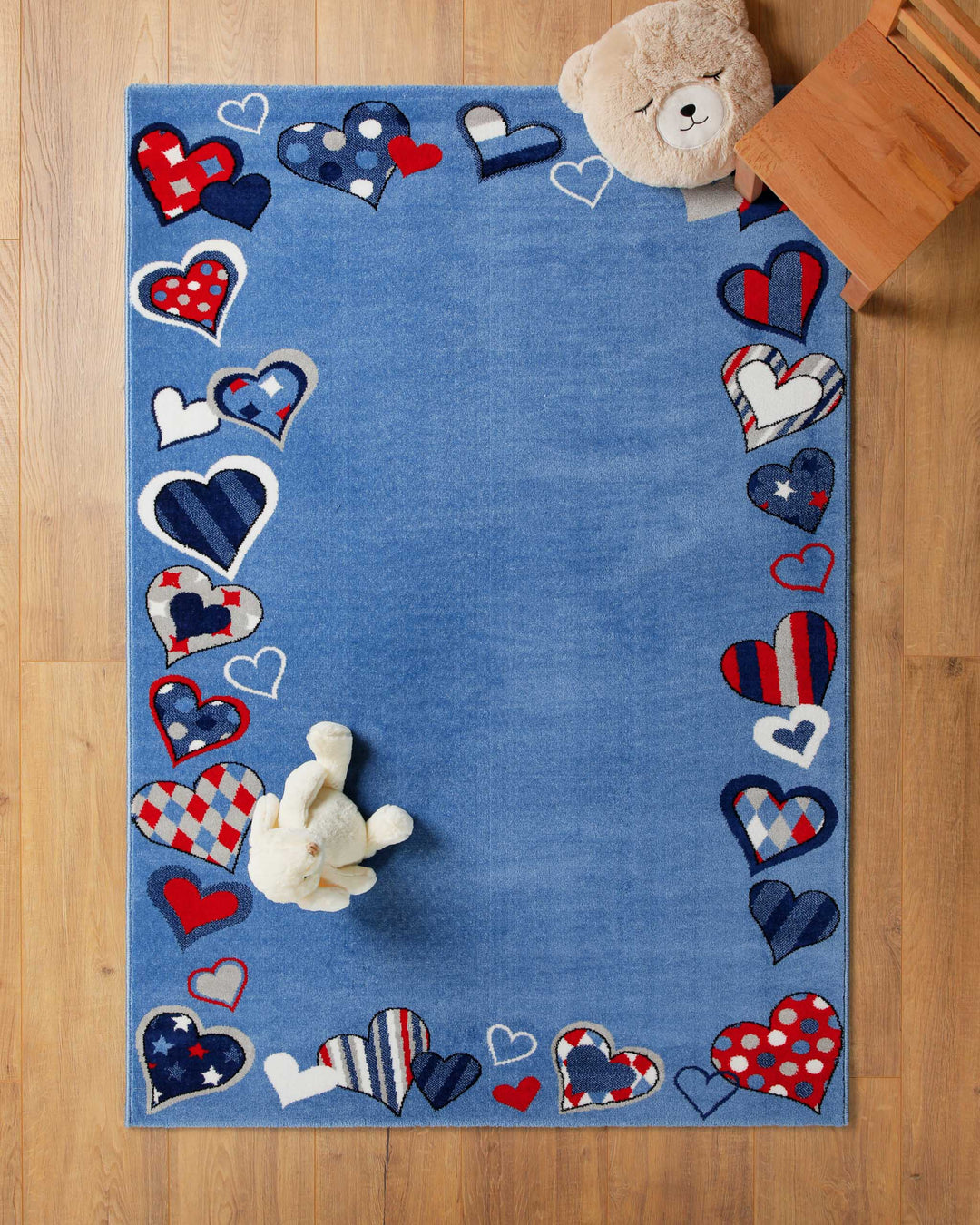 Kinderteppich Just Hearts in Blau auf Holzboden mit Teddybär in der Ecke, Patchwork-Rand mit Herz-Motiven