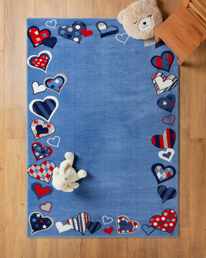 Kinderteppich Just Hearts in Blau auf Holzboden mit Teddybär in der Ecke, Patchwork-Rand mit Herz-Motiven