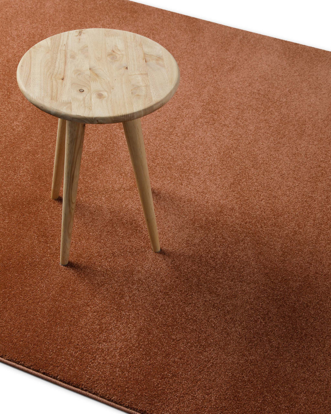 Kurzflor Teppich Freja Ziegel Rot im Wohnraum mit Hocker, zeigt warme Farbwirkung und Einsatz unter Möbeln
