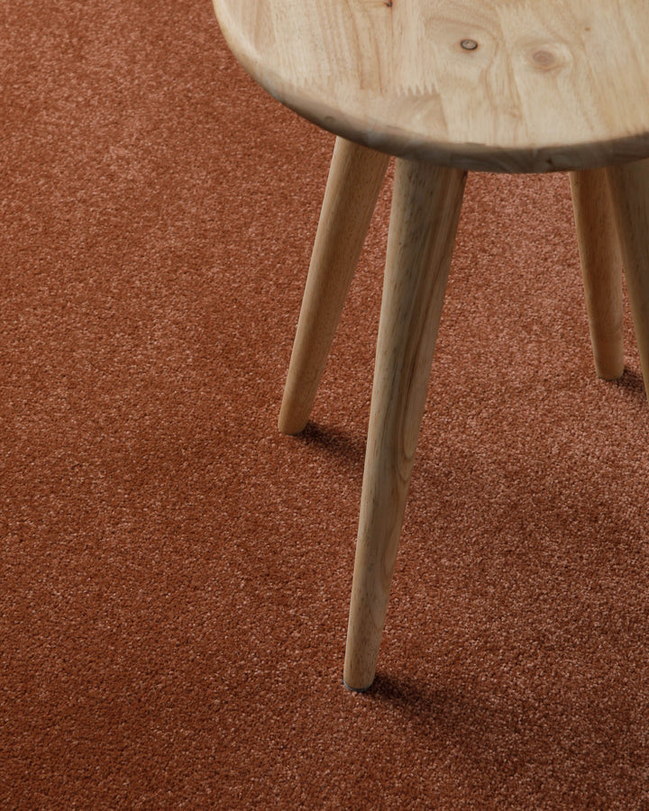 Kurzflor Teppich Freja Ziegel Rot Nahaufnahme mit Hockerbein, zeigt Oberfläche und Nutzung im Alltag