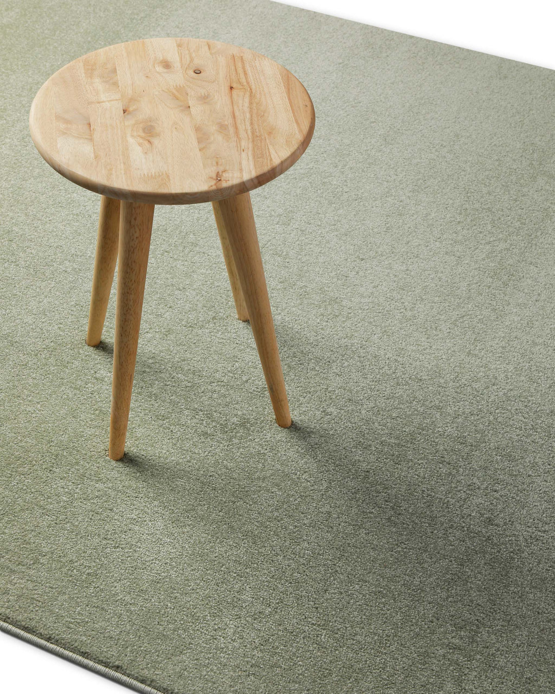 Kurzflor Teppich Freja Licht Grün im Wohnraum mit Hocker, zeigt Farbwirkung und Einsatz unter Möbeln