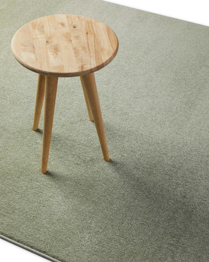 Kurzflor Teppich Freja Licht Grün im Wohnraum mit Hocker, zeigt Farbwirkung und Einsatz unter Möbeln