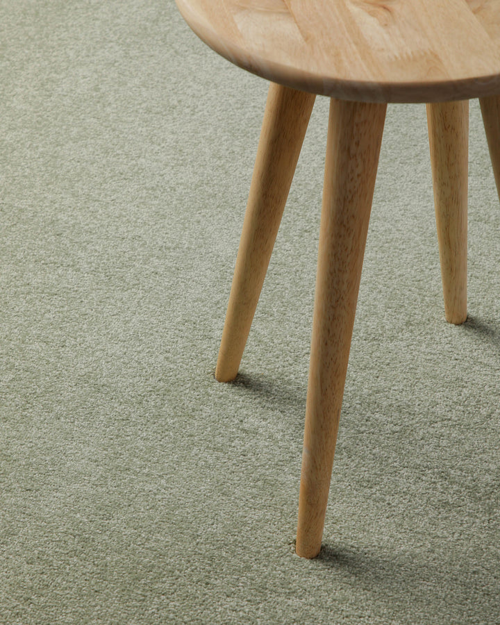 Kurzflor Teppich Freja Licht Grün Nahaufnahme mit Hockerbein, zeigt Oberfläche und Nutzung im Alltag