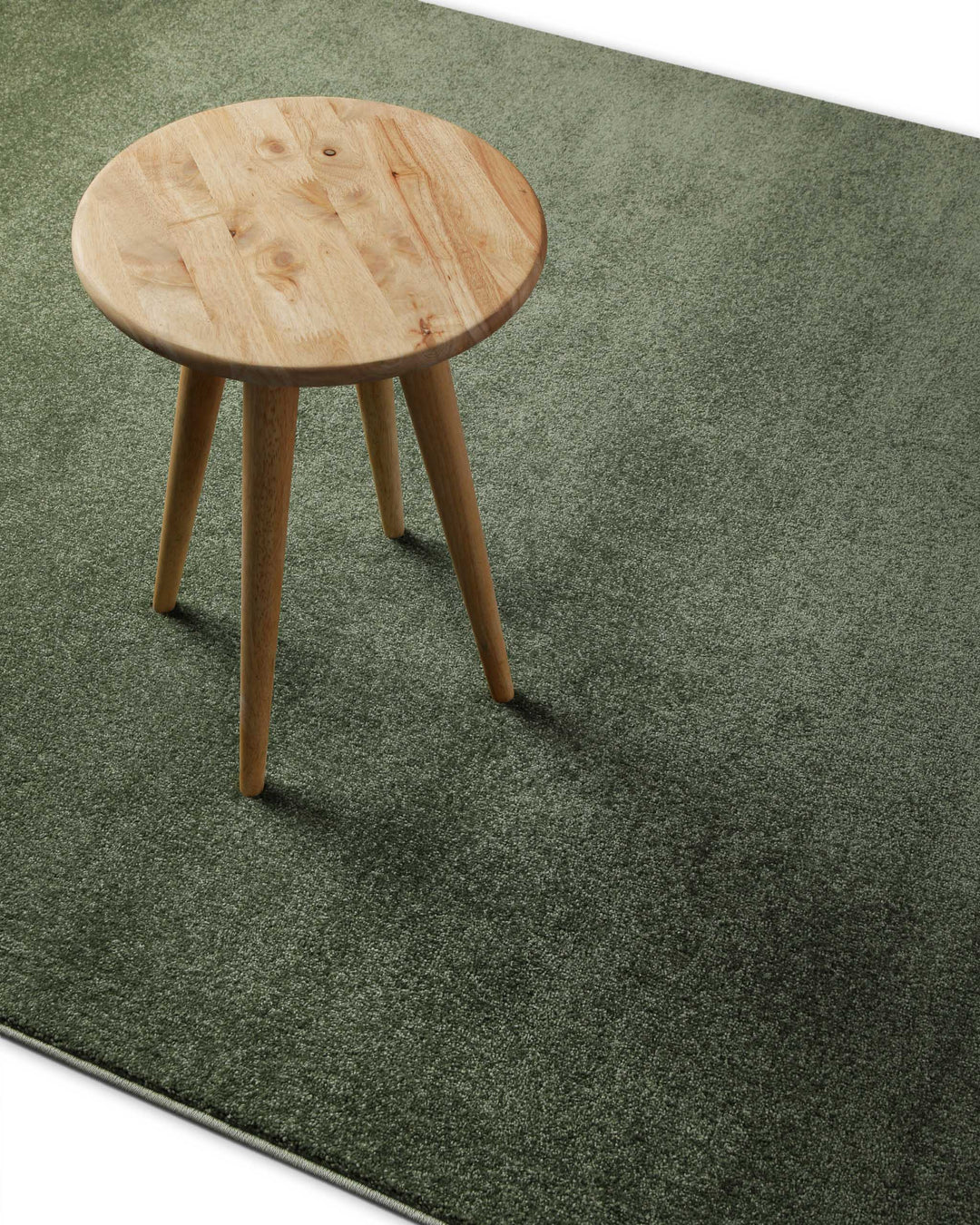 Kurzflor Teppich Freja Laub Grün im Wohnraum mit Hocker, zeigt natürliche Farbwirkung unter Möbeln