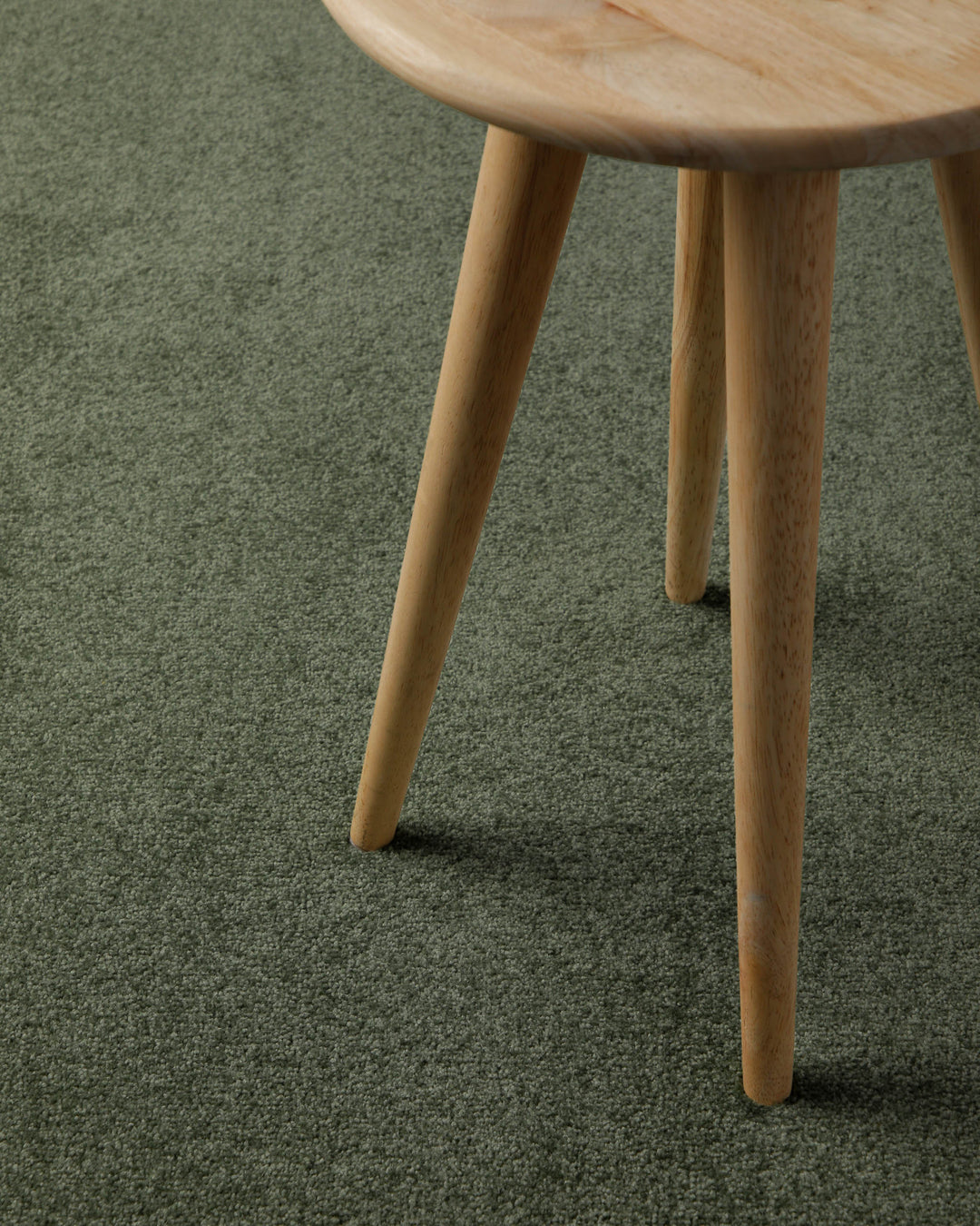 Kurzflor Teppich Freja Laub Grün Nahaufnahme mit Hockerbein, zeigt Oberfläche und Nutzung im Alltag