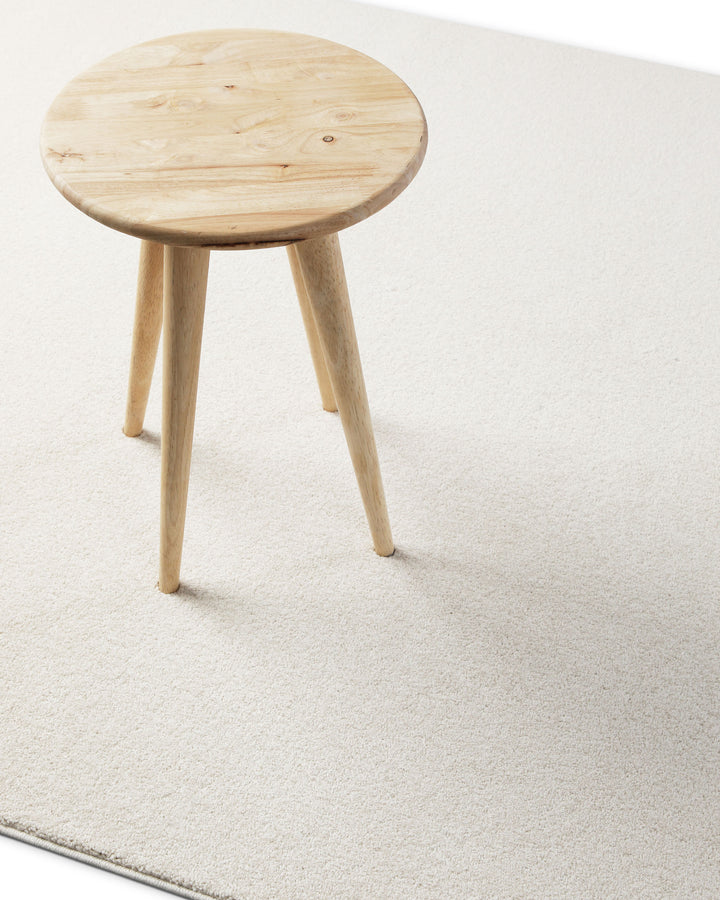 Kurzflor Teppich Freja Creme Weiß im Wohnraum mit Hocker, zeigt helle und ruhige Farbwirkung