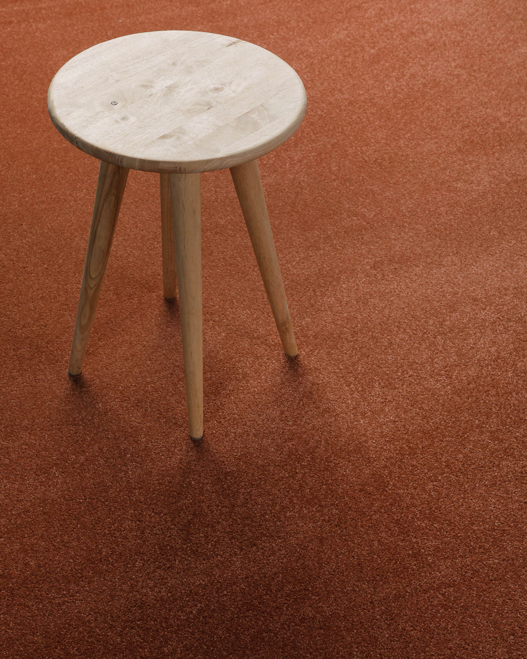 Kurzflor Teppich Montepulciano Ziegel Rot rund im Wohnraum mit Hocker auf warmer Oberfläche