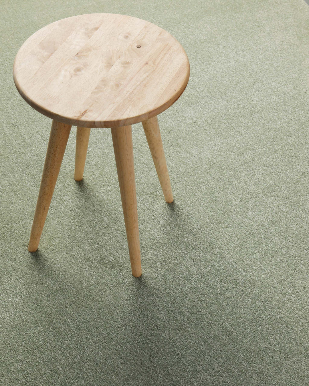 Kurzflor Teppich Montepulciano Lindgrün im Wohnraum mit Hocker auf ruhiger, natürlicher Oberfläche