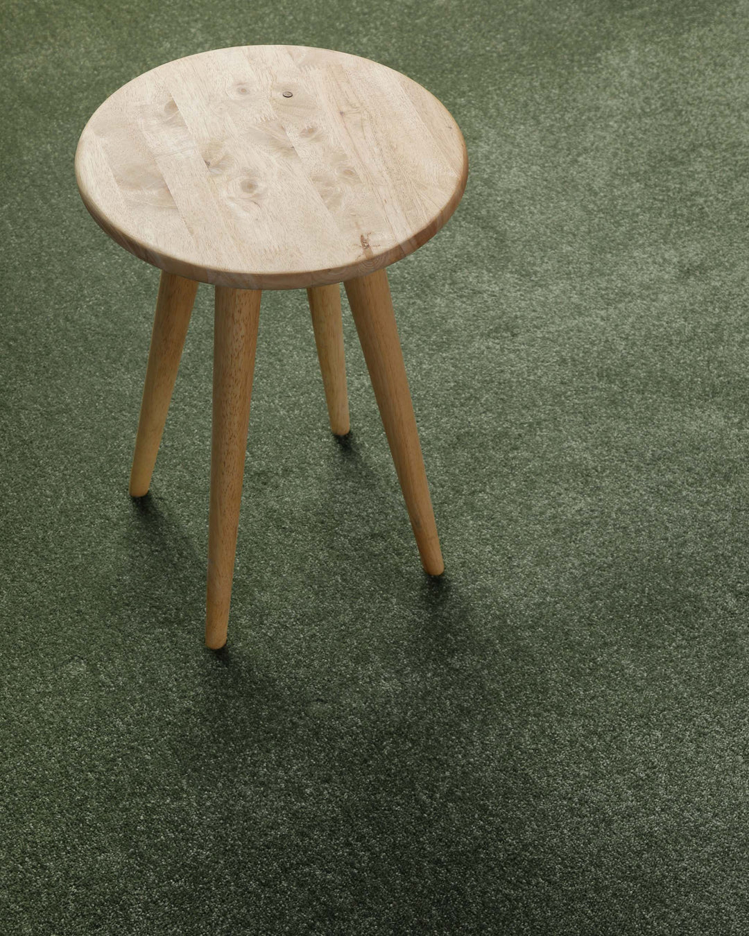 Kurzflor Teppich Montepulciano Laub Grün im Wohnraum mit Hocker auf Teppich