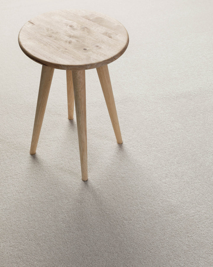 Kurzflor Teppich Montepulciano Creme Weiß im Wohnraum mit Hocker auf heller, ruhiger Oberfläche