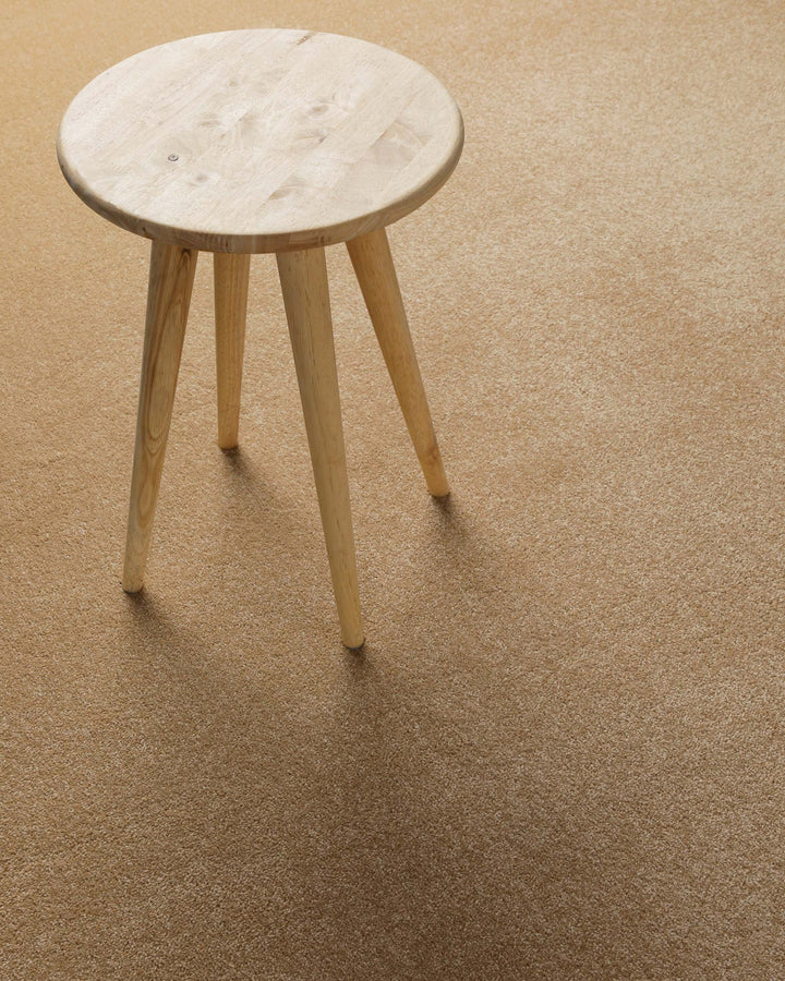 Kurzflor Teppich Montepulciano Sand Beige im Wohnraum mit Hocker auf warmer natürlicher Oberfläche