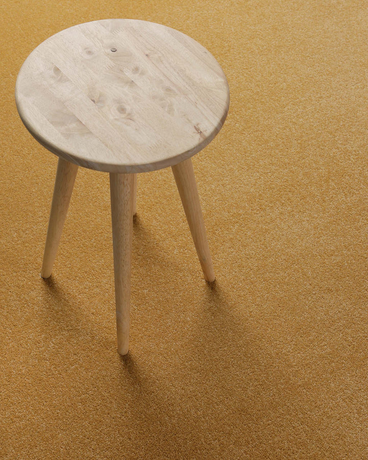 Kurzflor Teppich Montepulciano Ocker Gelb im Wohnraum mit Hocker auf warmer Oberfläche