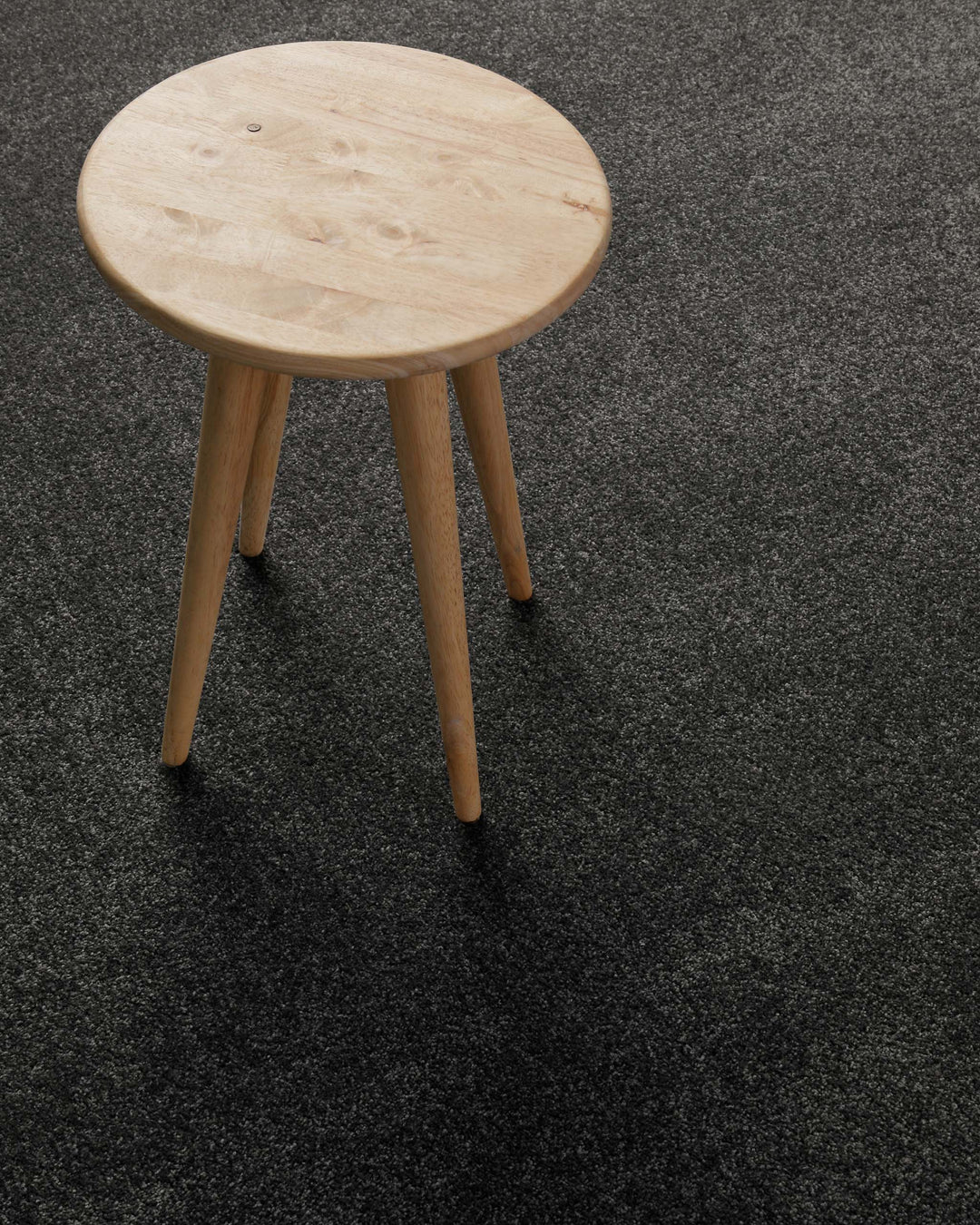 Kurzflor Teppich Montepulciano Anthrazit Grau im Wohnraum mit Hocker auf dunkler Oberfläche