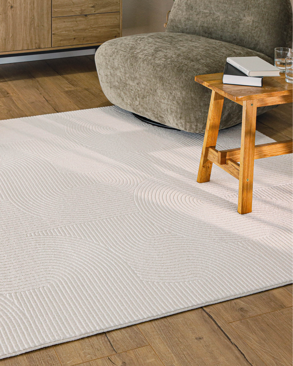 Nuuk Arc Kurzflorteppich creme-weiß im hellen Wohnzimmer mit Holztisch und Sessel