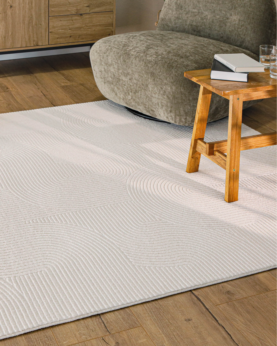 Nuuk Arc Kurzflorteppich creme-weiß im hellen Wohnzimmer mit Holztisch und Sessel