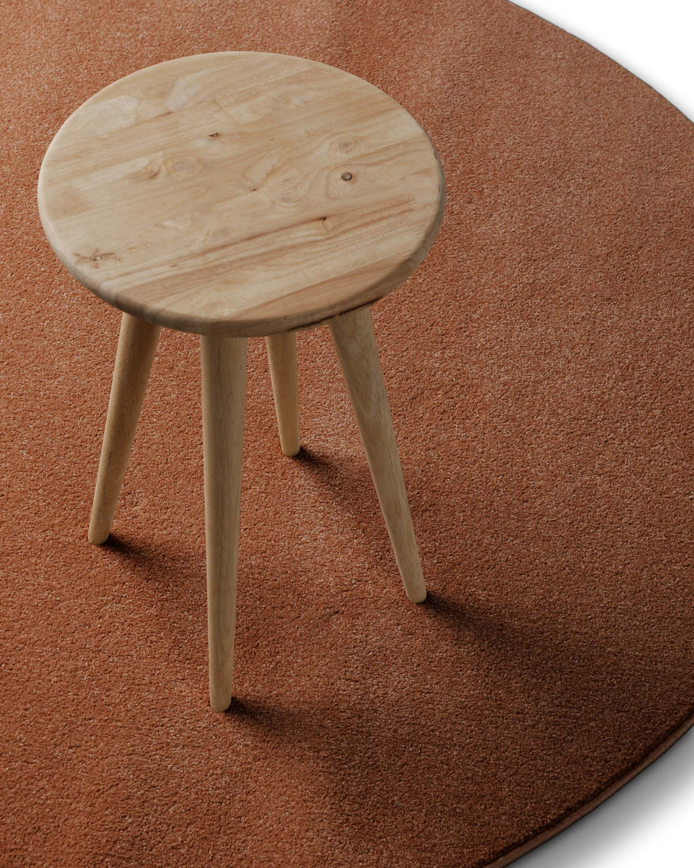 Kurzflor Teppich Freja Ziegel Rot rund im Wohnraum mit Hocker, zeigt Einsatz und Farbwirkung im Raum