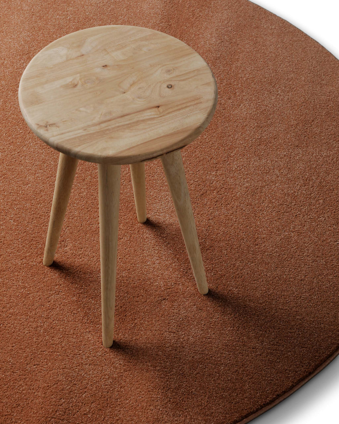 Kurzflor Teppich Freja Ziegel Rot rund im Wohnraum mit Hocker, zeigt Einsatz und Farbwirkung im Raum