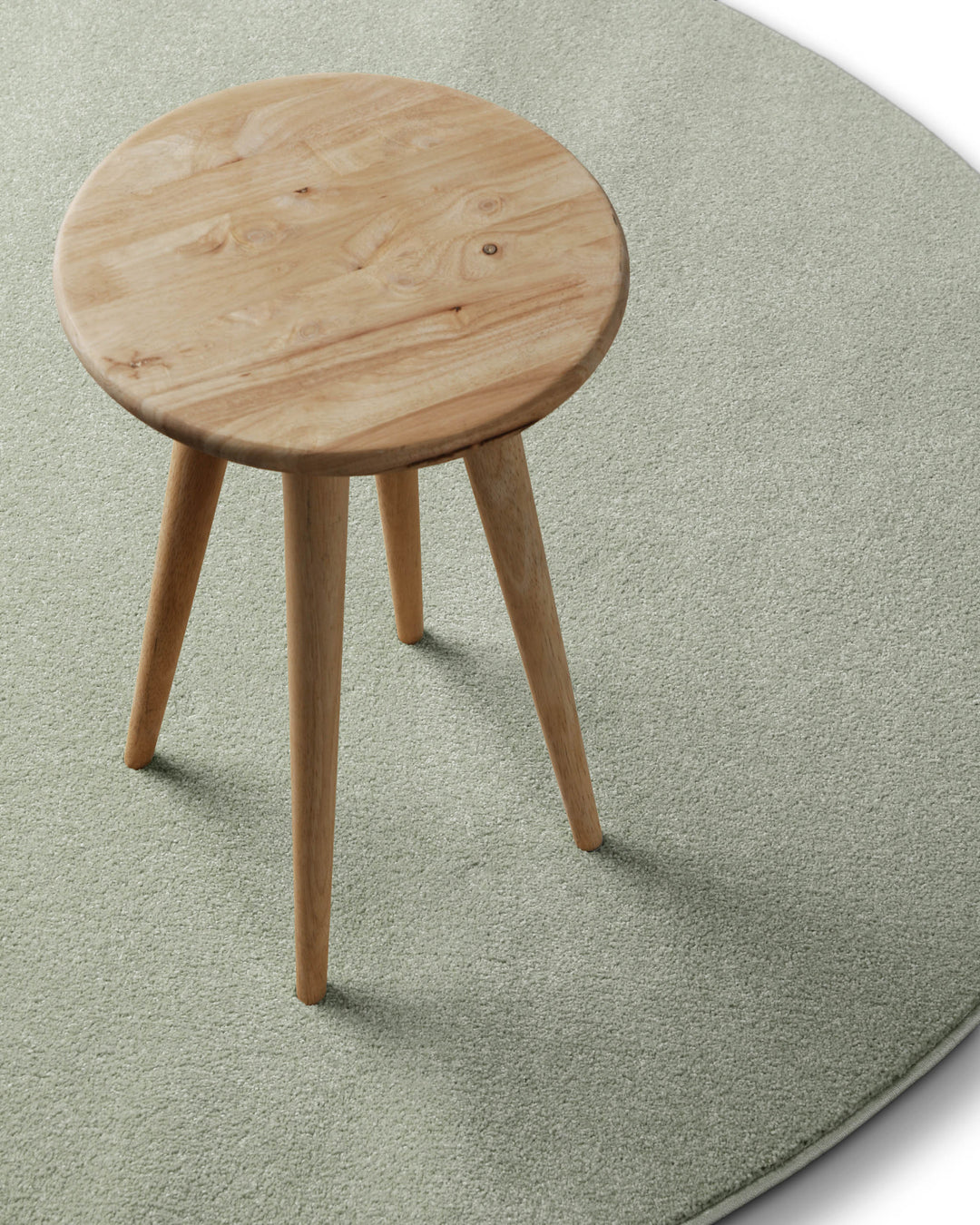 Kurzflor Teppich Freja Licht Grün rund im Wohnraum mit Hocker, zeigt Einsatz und Farbwirkung im Raum