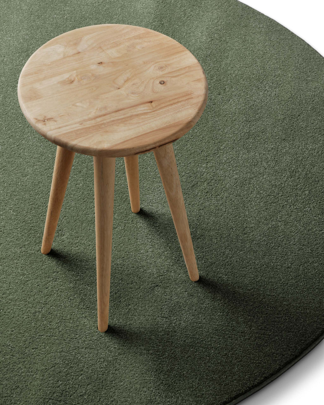 Kurzflor Teppich Freja Laub Grün rund im Wohnraum mit Hocker, zeigt natürliche Farbwirkung im Raum